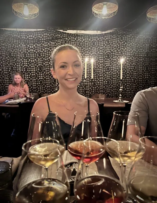 Ainsley Weliver smiling at a table with multiple wine glasses.