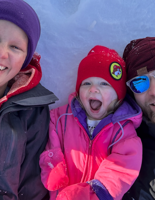 Dan Wist smiling in snow with two others, one child in a red hat.