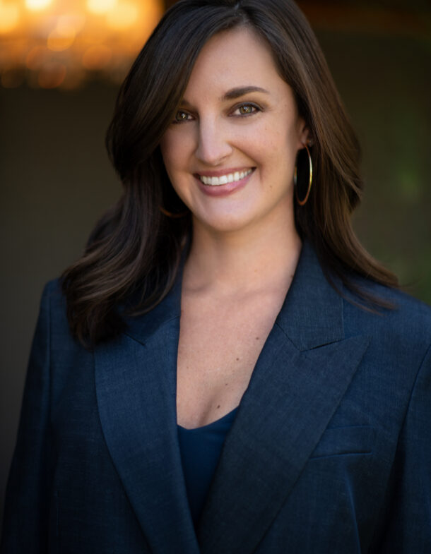 Hilary Hadden in a dark blazer with hoop earrings against a softly lit, blurred background