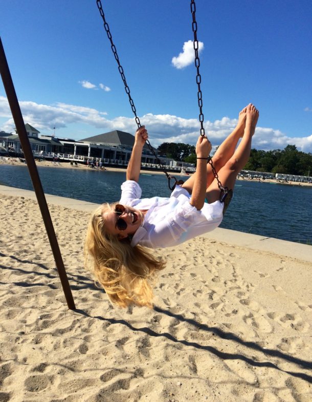 Person on swing near water, smiling, sunny day